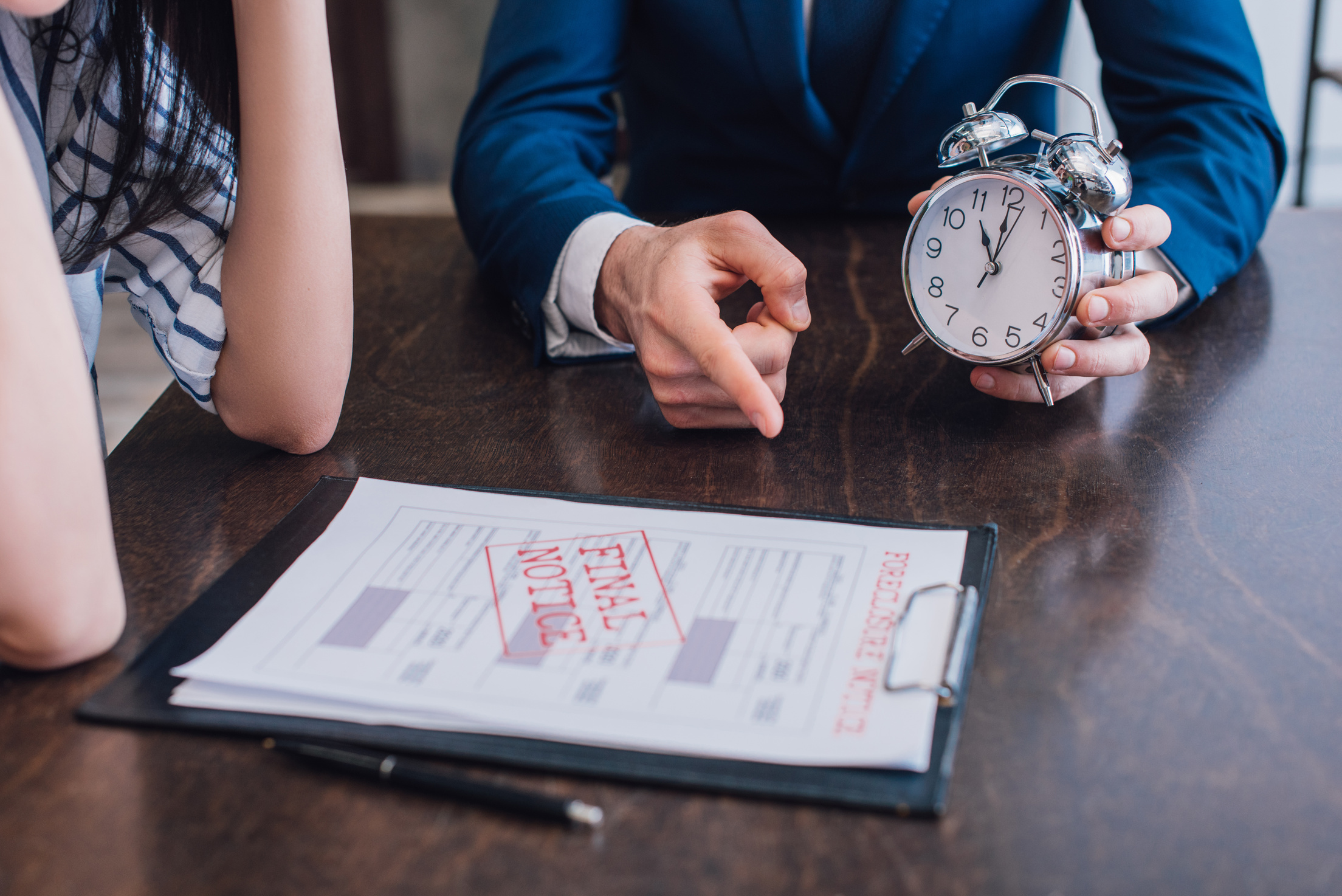 Cropped view of collector with alarm clock pointing at documents with foreclosure and final notice lettering near woman at table